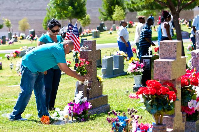 Following the 48th Annual Memorial Day Service, Trini and Paula Torres place flowers and American flags on a grave of their loved one at the Palm Downtown Mortuary and Cemetery in Las Vegas, Monday, May 27, 2013.